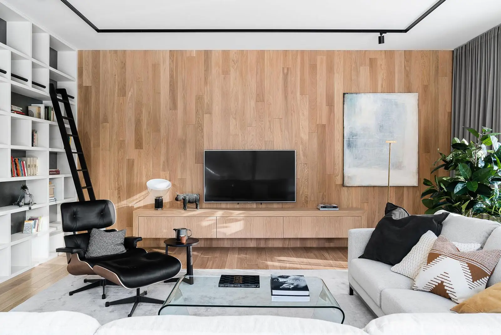 Przytulny salon z wbudowaną biblioteczką, telewizorem, czarnym fotelem wypoczynkowym i neutralnymi tonacjami w luksusowym apartamencie w Gdańsku