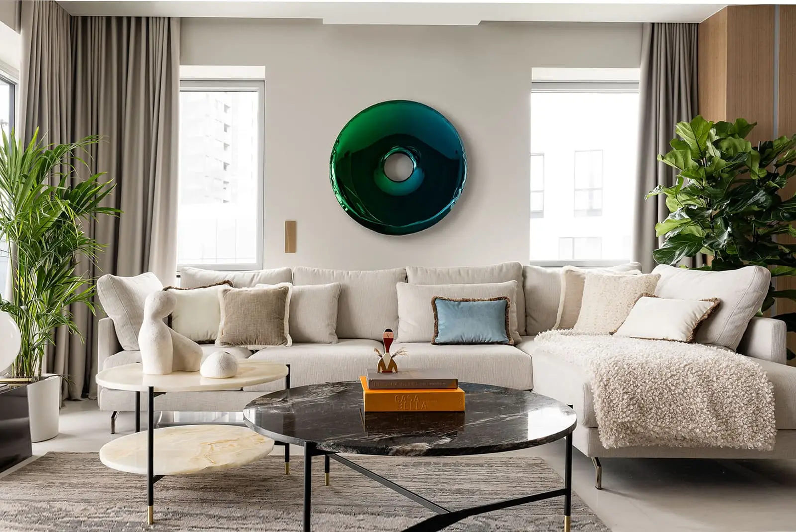 Przestronny salon z beżową sofą narożną, marmurowymi stolikami kawowymi i zielonym okrągłym dziełem sztuki w luksusowym designie w Gdańsku