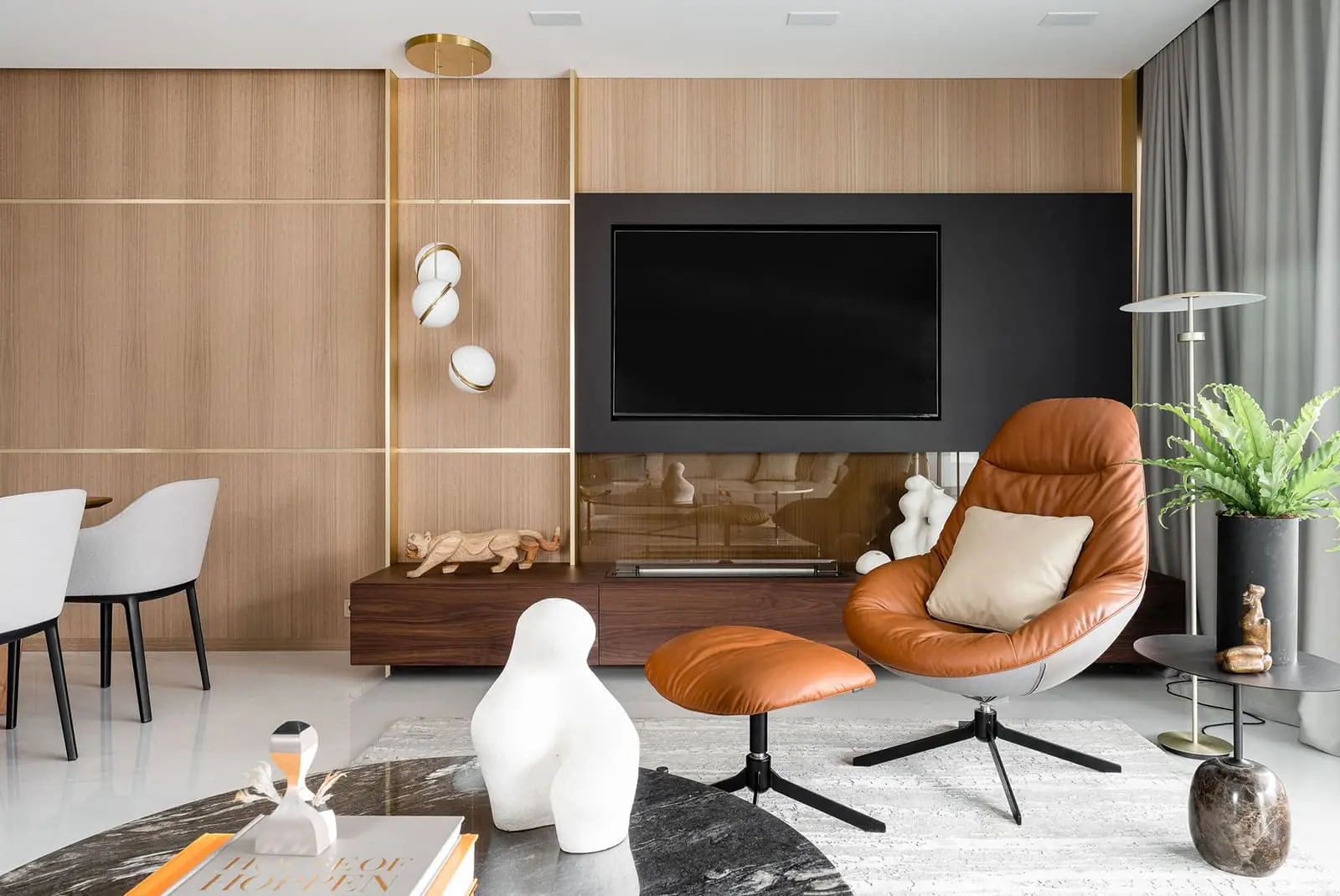 Stylowy salon z pomarańczowym skórzanym fotelem, ścianą z telewizorem i abstrakcyjnymi rzeźbami w premium aranżacji wnętrz w Gdańsku