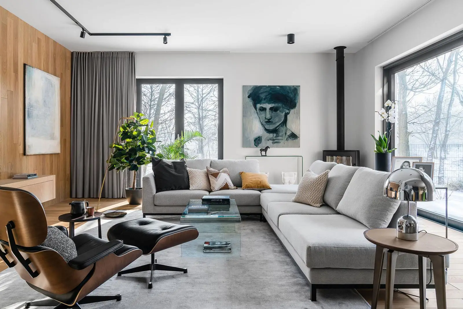Nowoczesny salon z szarą sofą w kształcie L, drewnianymi akcentami, roślinami i widokiem na zimowy krajobraz w Gdańsku